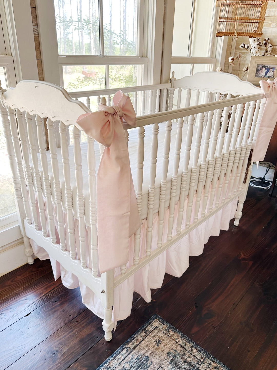Angled view of the crib with both pink sashes and the gathered pink skirt falling to the floor