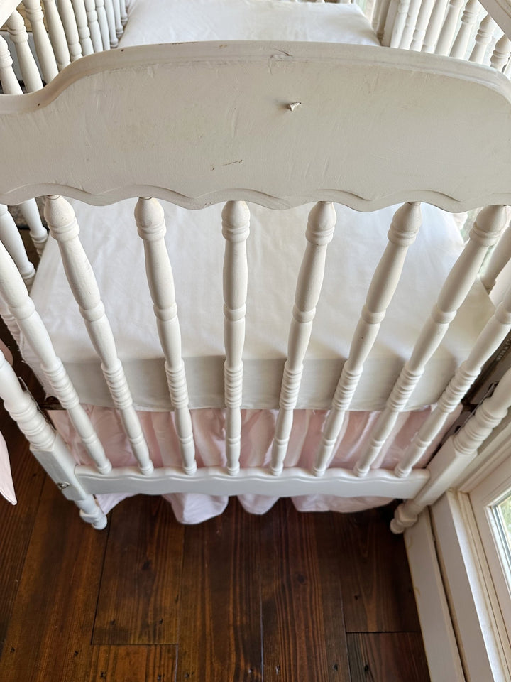 The scalloped headboard and turned spindles above the baby pink farmhouse skirt