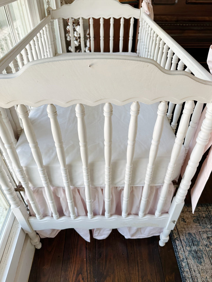 Looking down at the crib from the head end, white sheet above the soft pink gathers