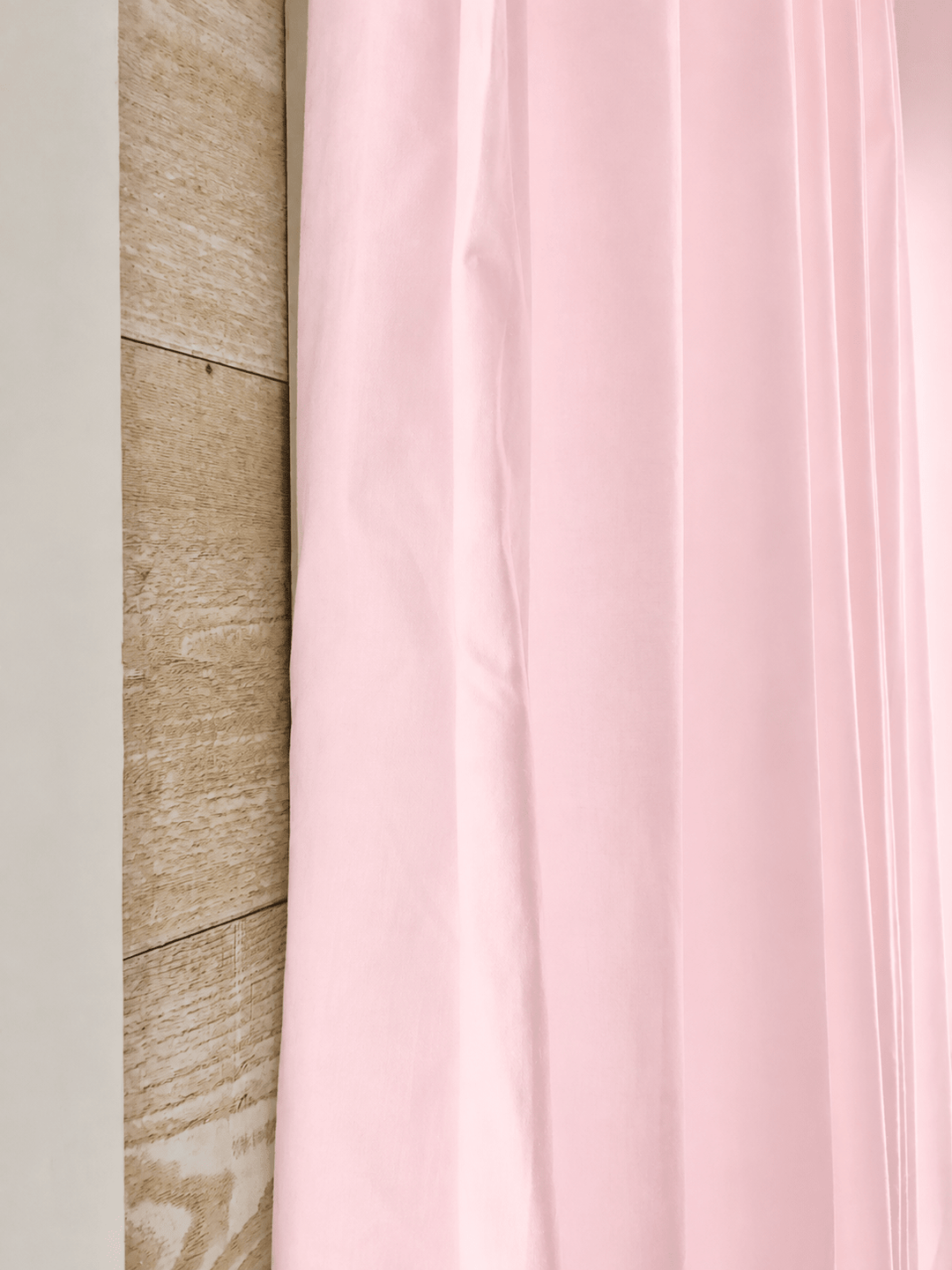 Edge of a baby pink farmhouse curtain panel against pale shiplap, showing the washed cotton and the tailored flat edge - High Cotton Textile
