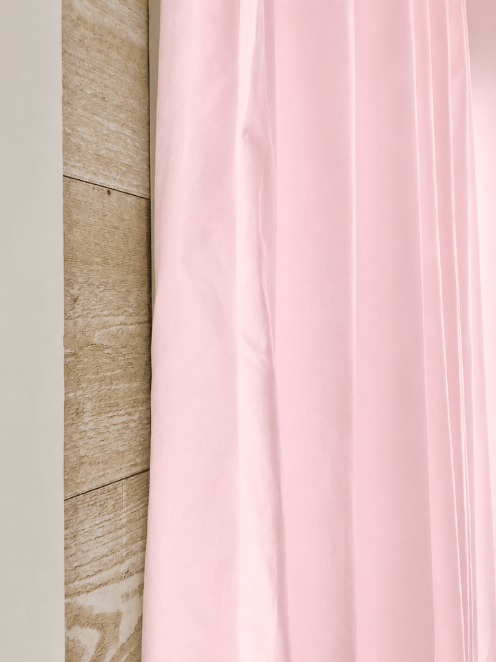Edge of a baby pink farmhouse curtain panel against pale shiplap, showing the washed cotton and the tailored flat edge - High Cotton Textile