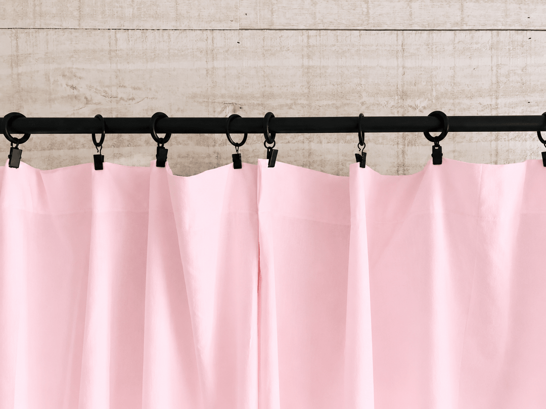 Baby pink farmhouse curtain panels hanging in soft folds from black clip rings across a rod - High Cotton Textile