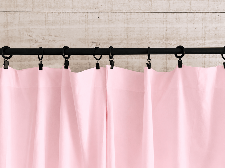 Baby pink farmhouse curtain panels hanging in soft folds from black clip rings across a rod - High Cotton Textile
