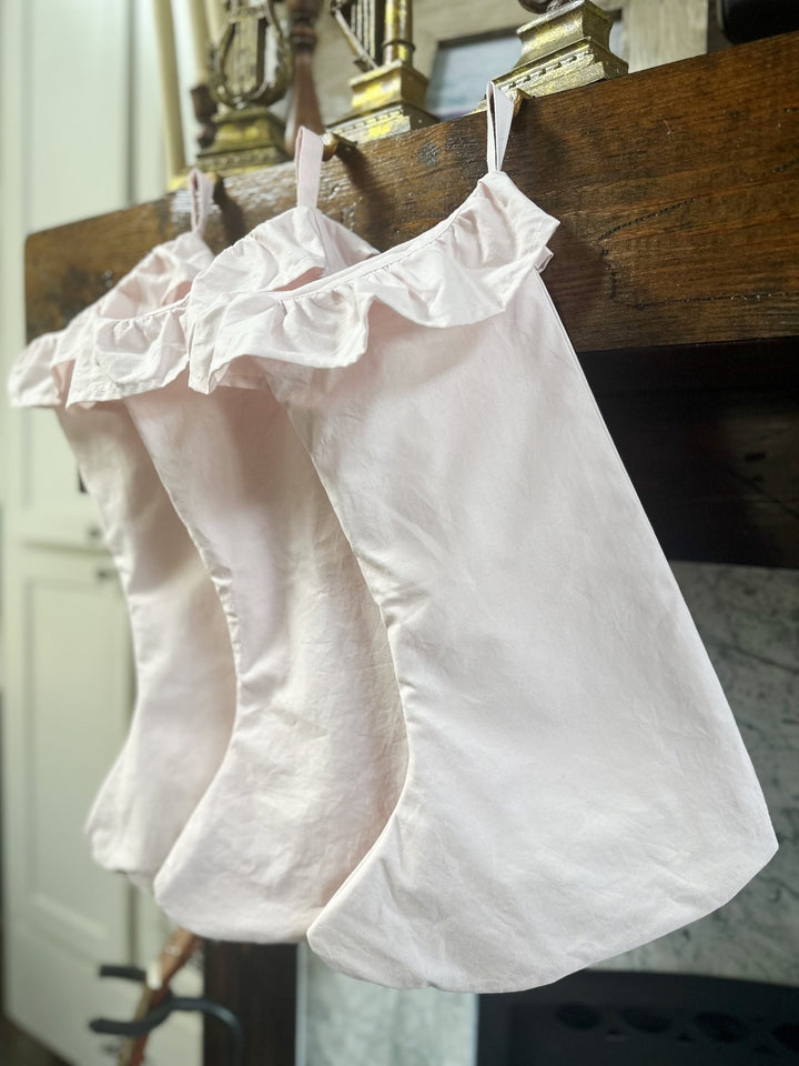 Angled view of pink ruffled stockings hanging from cotton loops on a wood mantel