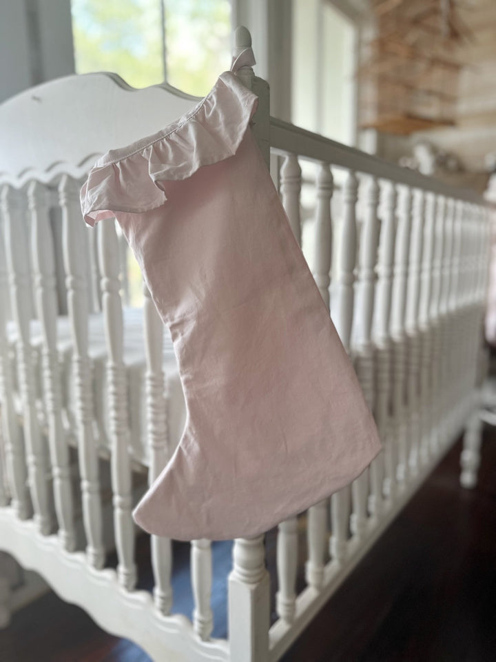 Single baby pink farmhouse stocking hanging on a white spindle crib in a sunny nursery