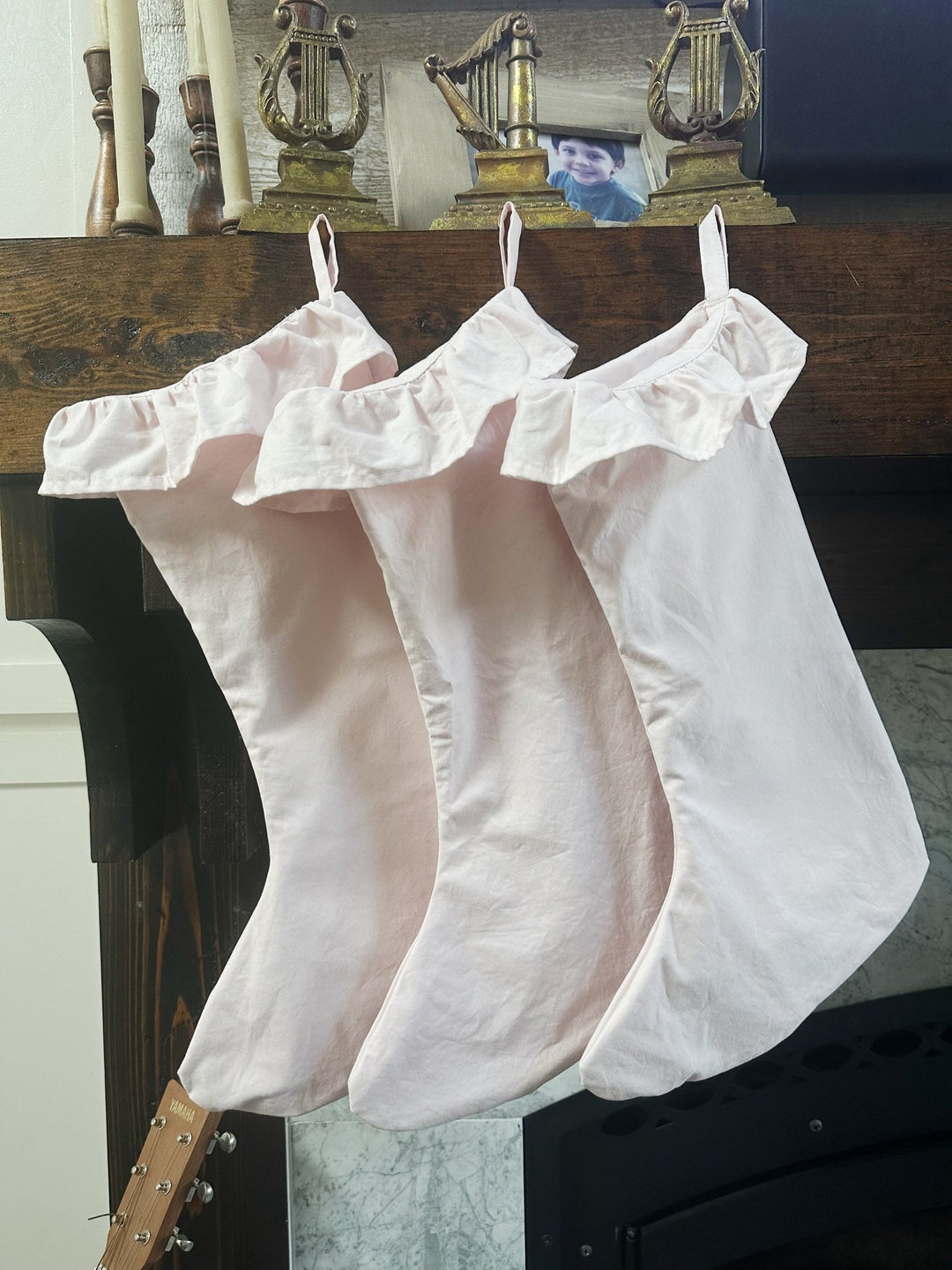 Three baby pink ruffled Christmas stockings hanging from a dark wood mantel below gold candlesticks