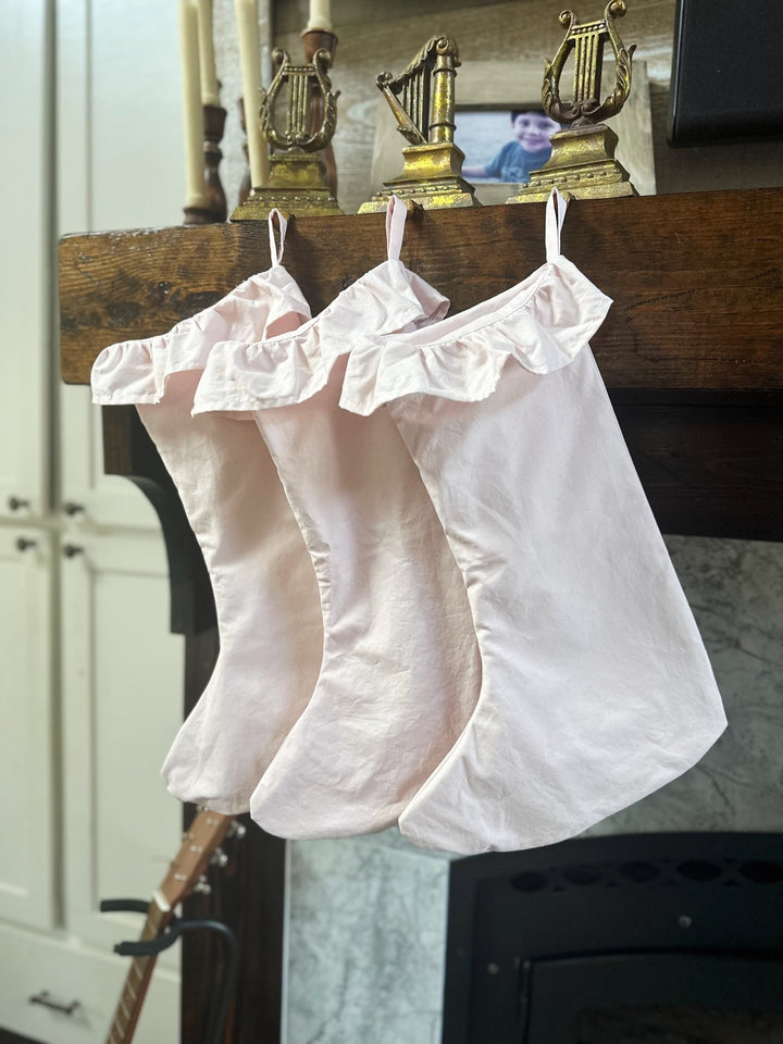 Baby pink Christmas stockings with gathered ruffle cuffs hanging side by side from a mantel