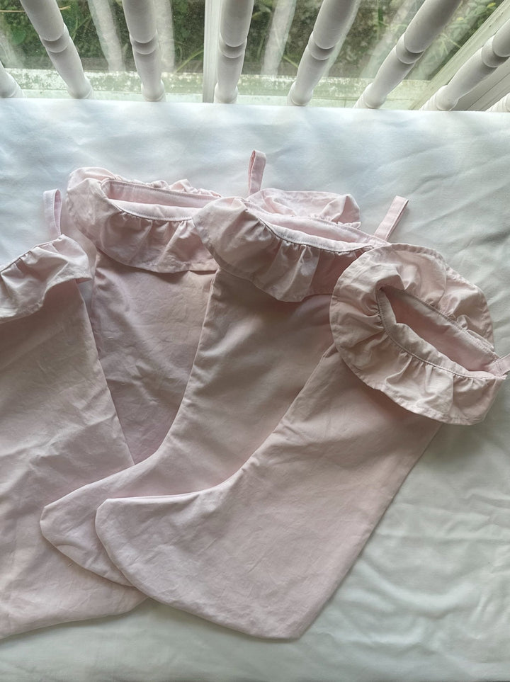 Three baby pink ruffled stockings laid flat on a white crib mattress, showing the ruffle cuffs and loops