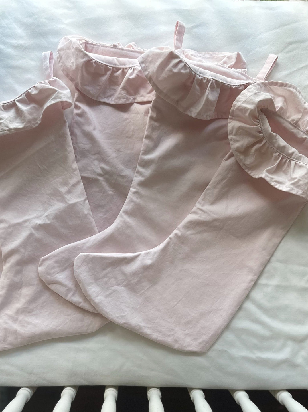 Pink ruffled Christmas stockings laid on a crib mattress beside white crib spindles