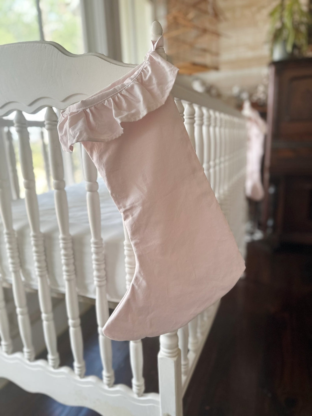 Baby pink ruffled stocking hung on a white crib rail for baby's first Christmas