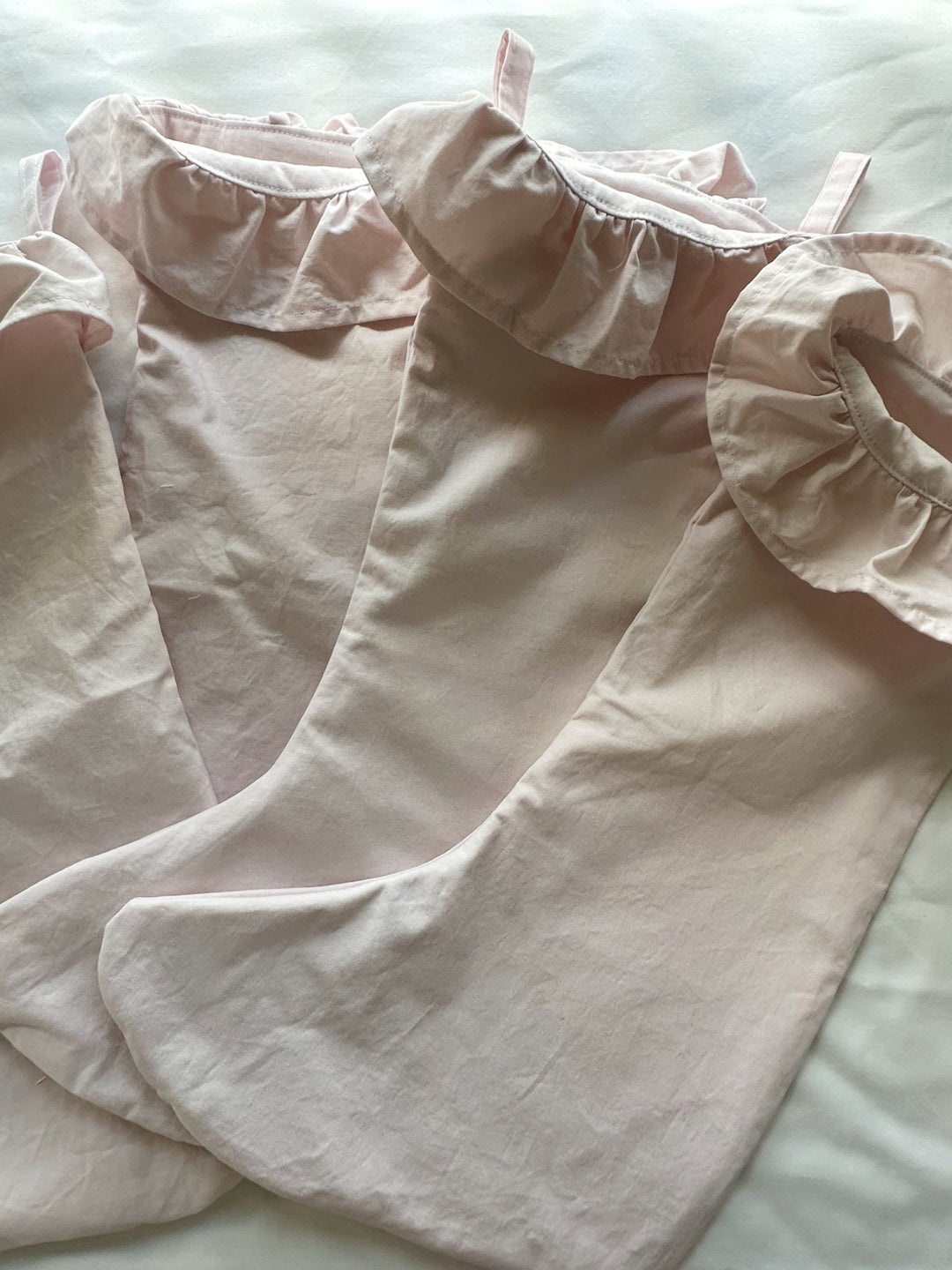 Close-up of baby pink washed cotton stockings and ruffled cuffs laid on white bedding