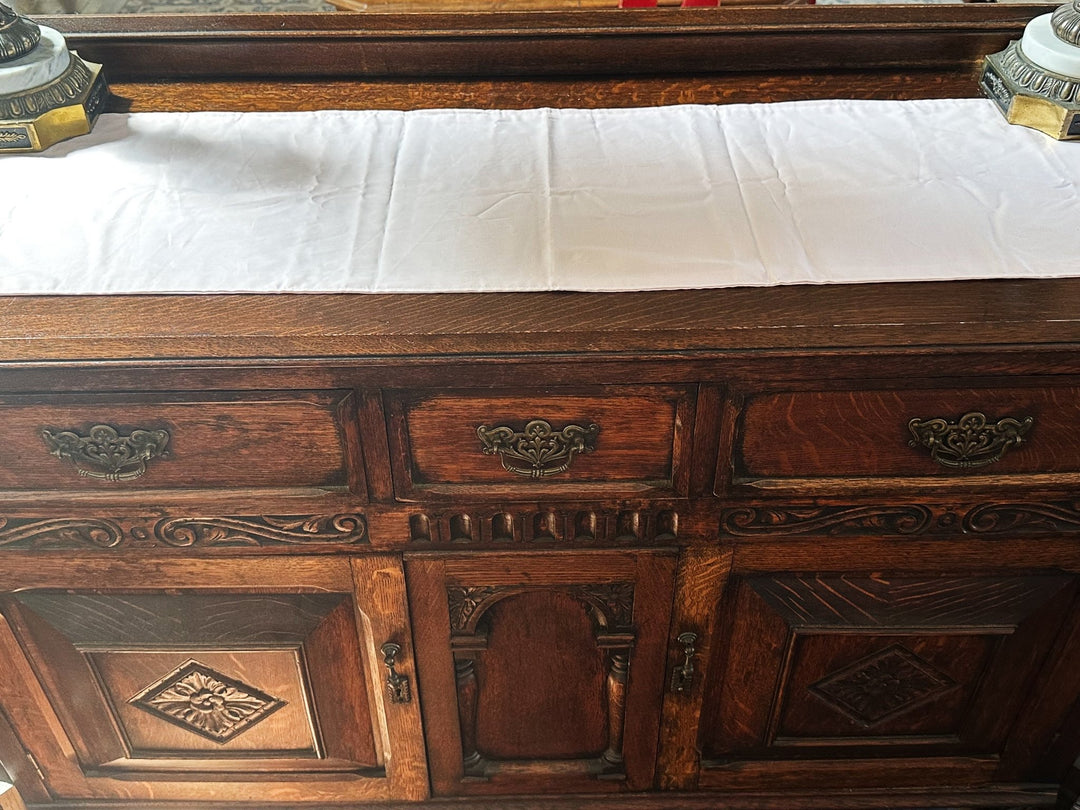Baby pink cotton runner laid along the top of a carved oak sideboard between two marble and brass lamps