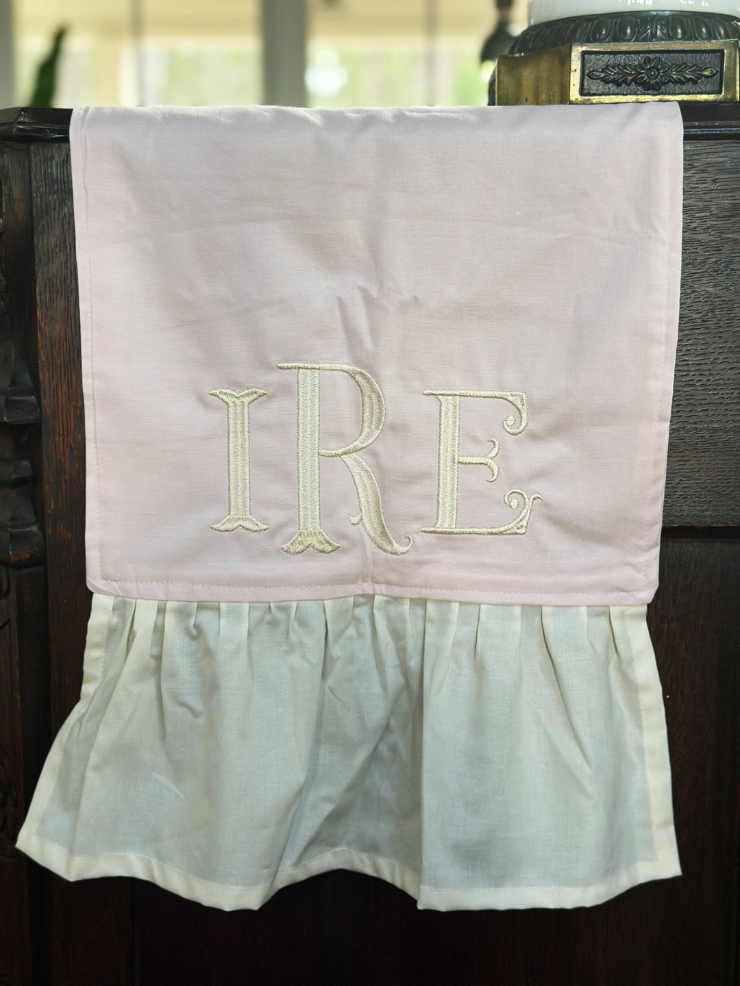 Close-up of a cream three-letter monogram embroidered on the baby pink runner just above the ivory ruffle