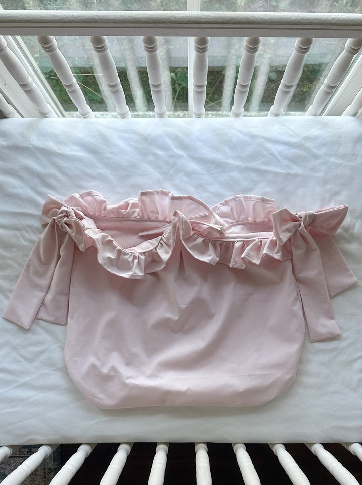 Baby pink ruffled crib caddy laid flat with its gathered ruffle opening and bow ties