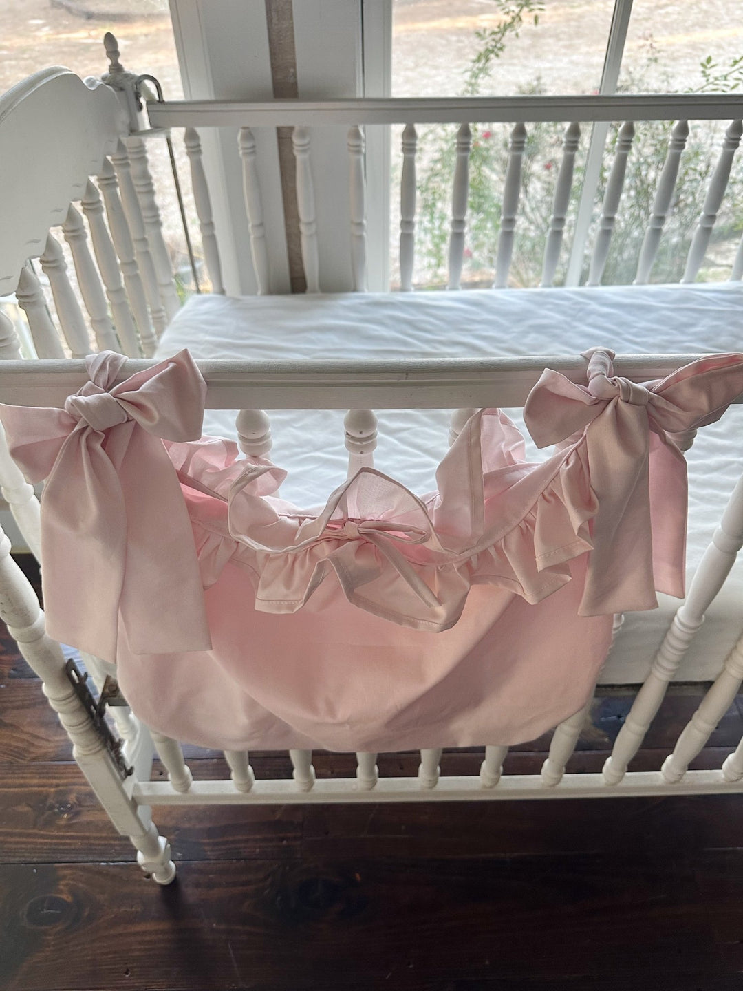 Baby pink caddy seen from above the crib, two pink bows tied around the rail