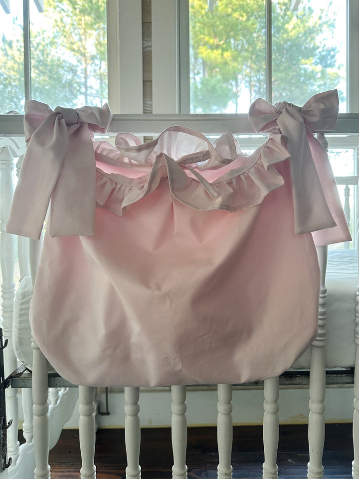 Baby pink ruffled hanging crib caddy tied to a white crib rail with two big pink sash bows