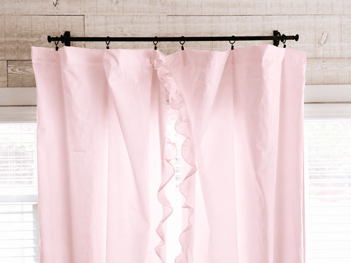 Top of the baby pink ruffled curtain panels on iron rings, showing the gathered heading against shiplap - High Cotton Textile