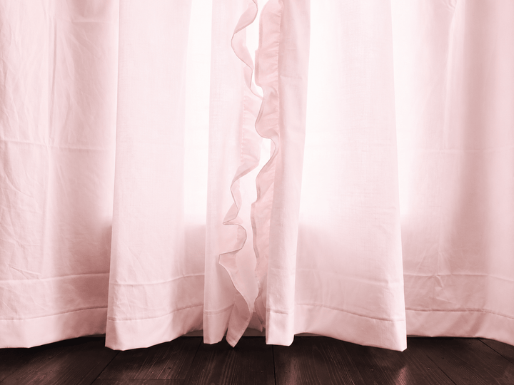 Hem of the baby pink ruffled nursery curtains where the panels meet the dark wood floor - High Cotton Textile