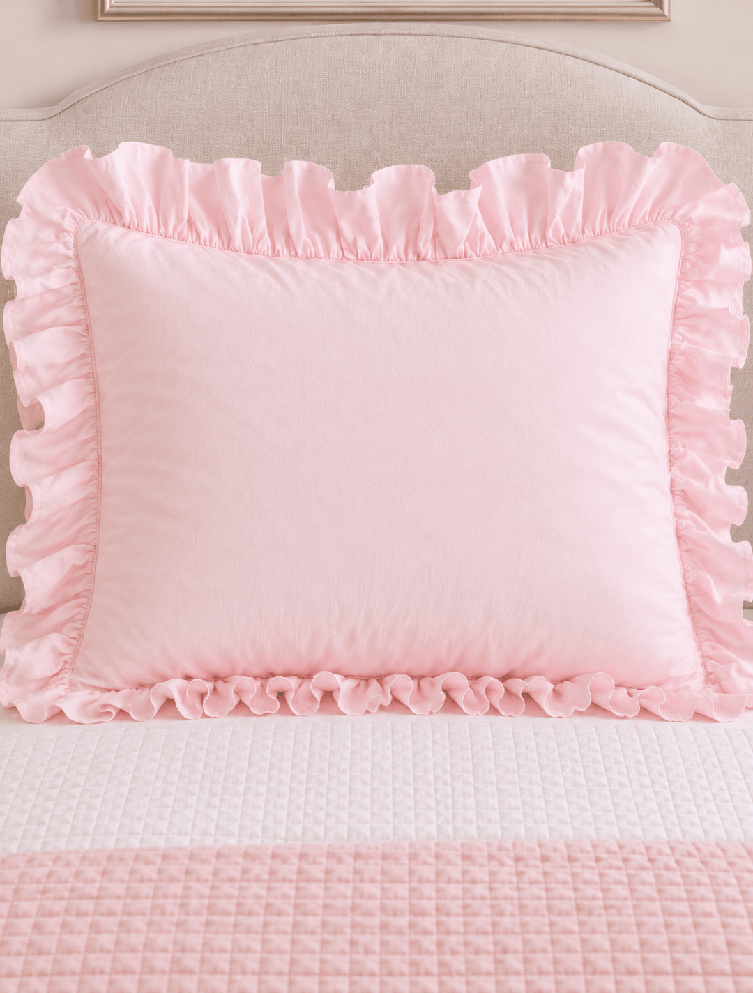 Baby pink ruffled pillow sham centered on a twin bed against a linen headboard - High Cotton Textile