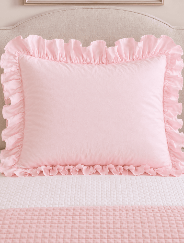 Baby pink ruffled pillow sham centered on a twin bed against a linen headboard - High Cotton Textile
