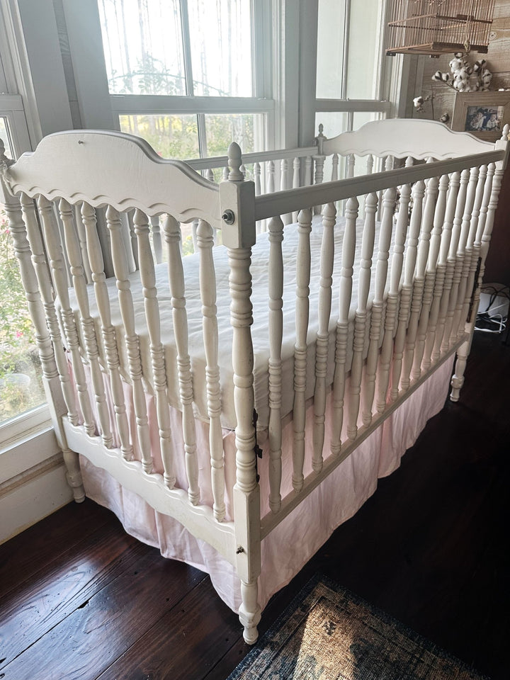 Corner angle of the baby pink tailored crib skirt hanging straight to the floor beneath a white crib