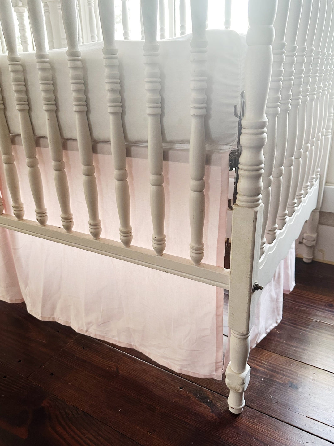 Split corner of the baby pink tailored skirt wrapping cleanly around the crib leg