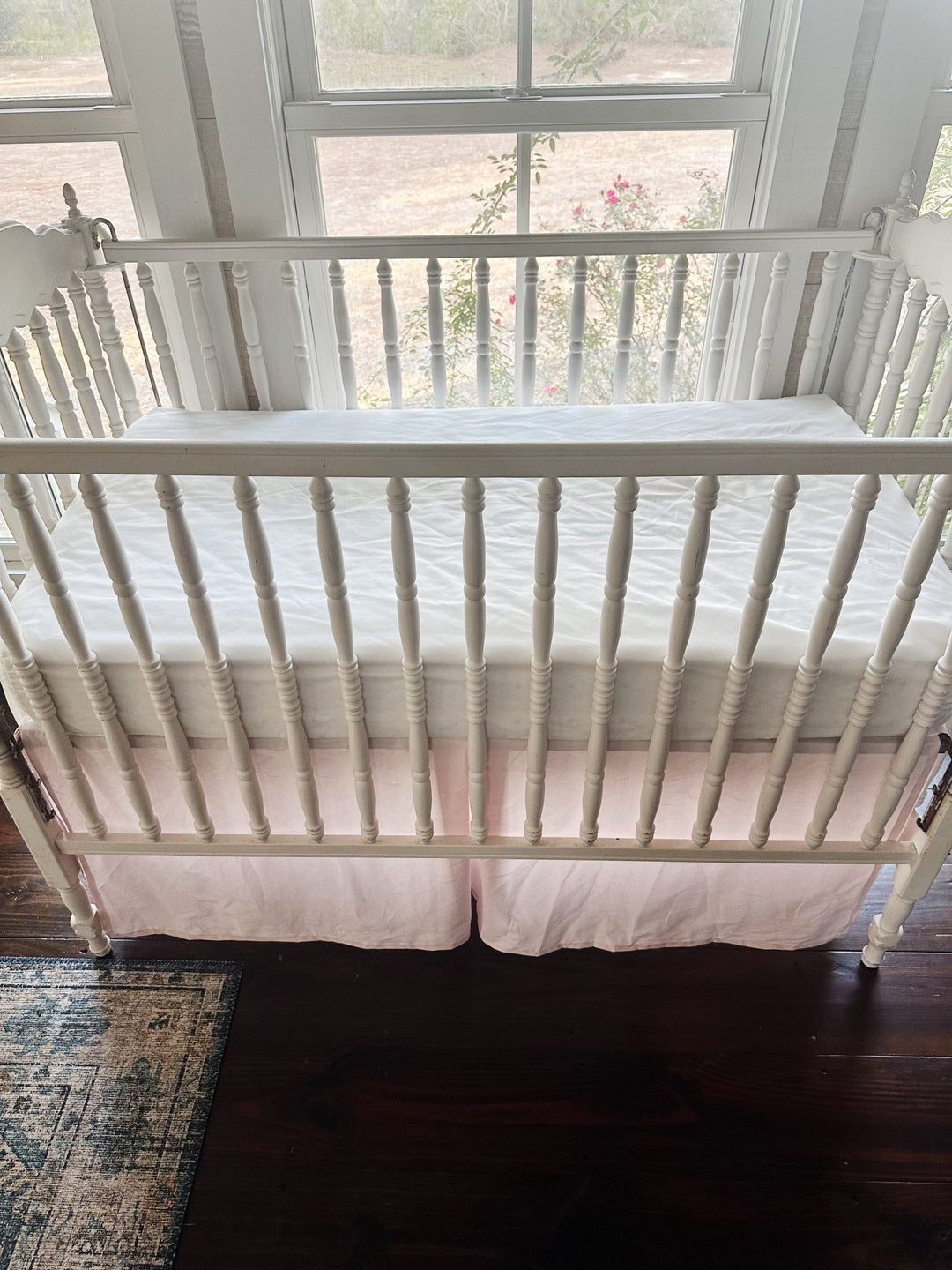 Looking down over the crib rail at the pleated baby pink skirt below a white fitted crib sheet