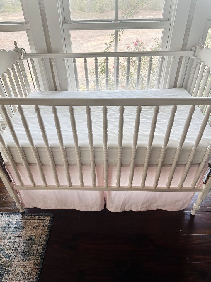 Looking down over the crib rail at the pleated baby pink skirt below a white fitted crib sheet