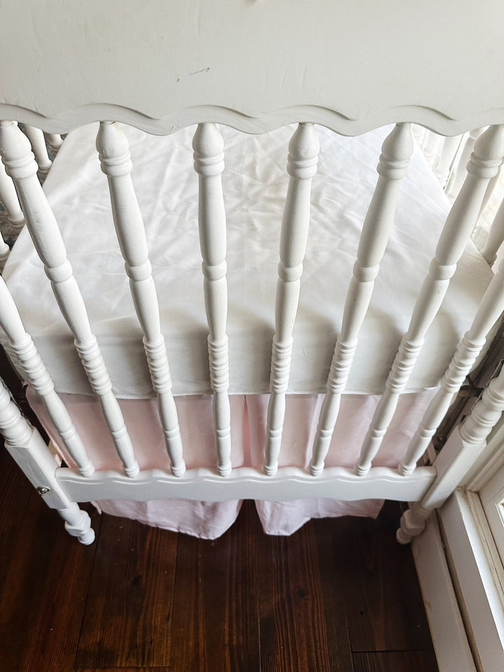 Short side of the baby pink tailored crib skirt with a center pleat, seen through the crib spindles
