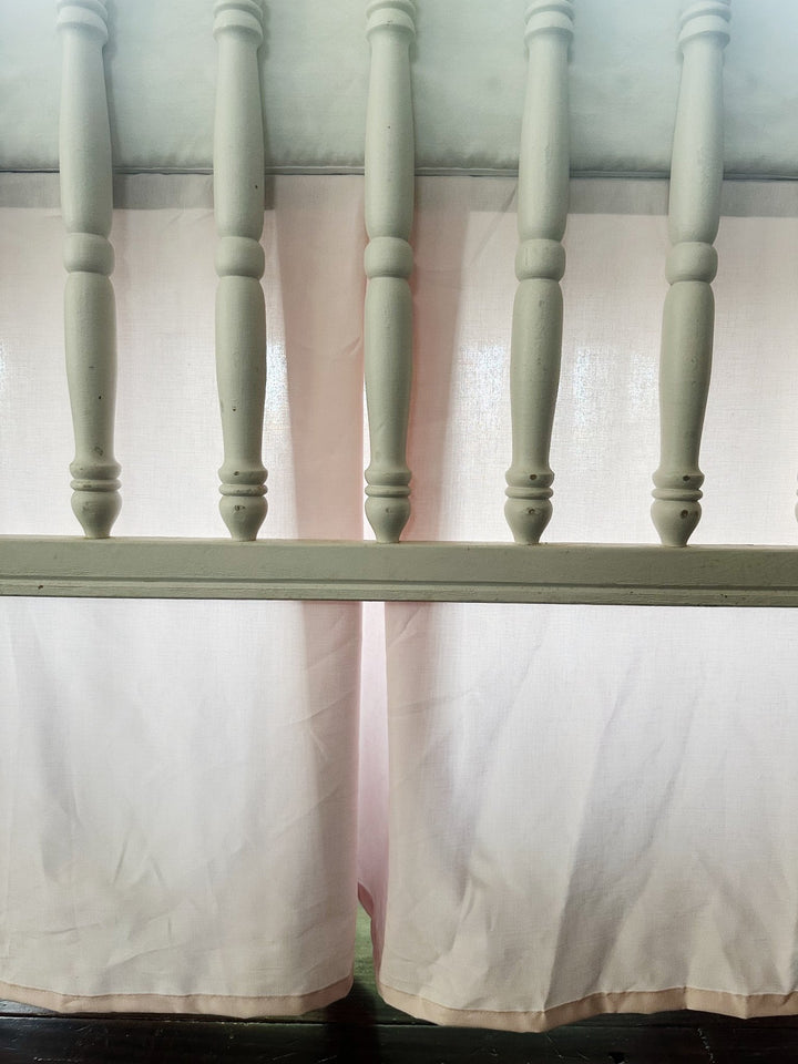 Close-up of the baby pink pleat and hemmed edge through white crib spindles