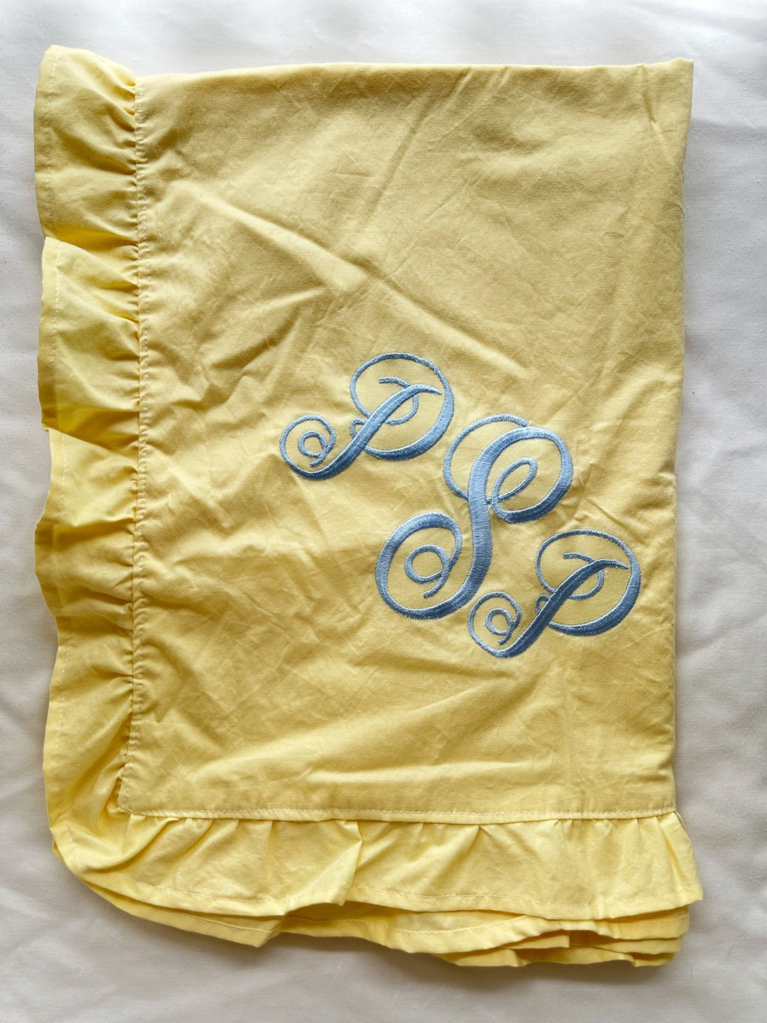 Folded baby yellow ruffled crib blanket with a baby blue script monogram in washed cotton - High Cotton Textile