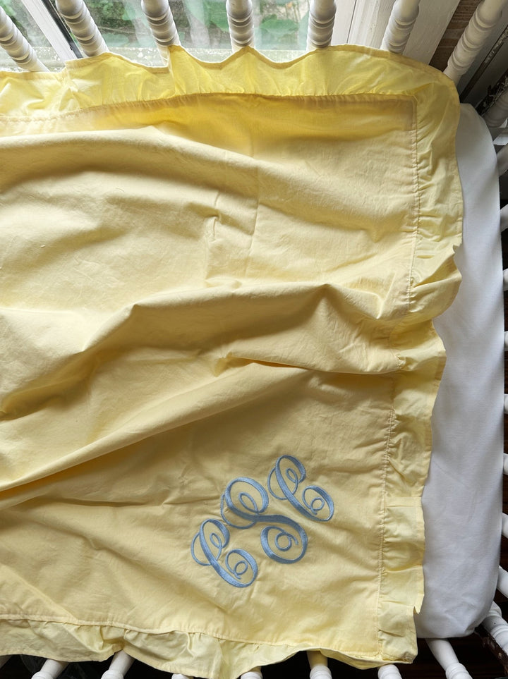 Close up of the ruffle edge and blue monogram on a handmade yellow cotton baby blanket - High Cotton Textile
