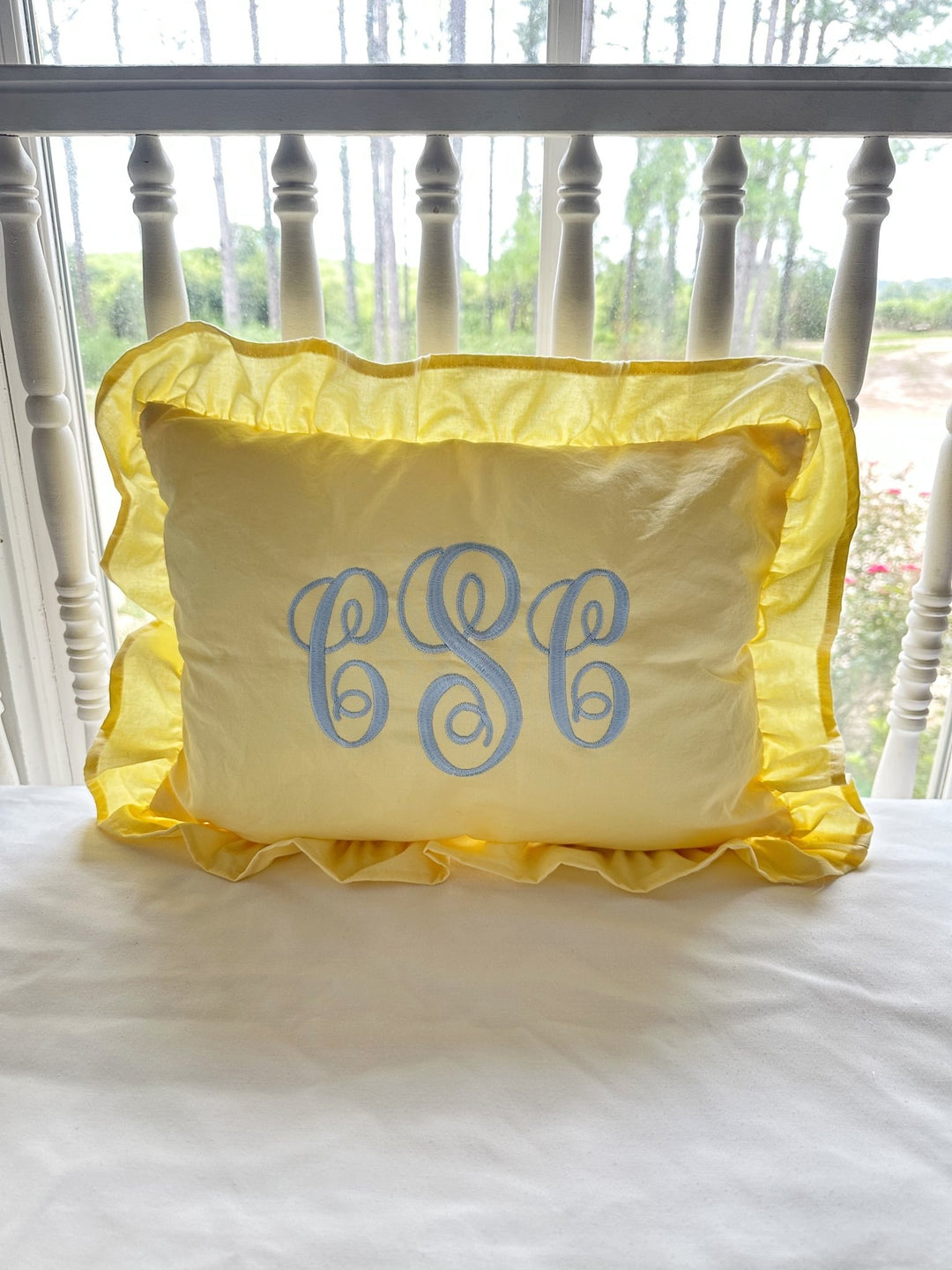 Baby yellow ruffled crib pillow with a blue script monogram on a white spindle crib - High Cotton Textile