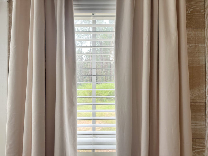 Ballet Slipper Pink panels parted to frame a narrow window with white wood blinds and pine trees outside