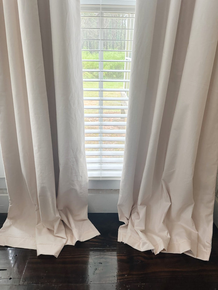 Bottom of two Ballet Slipper Pink blackout panels puddling softly on a dark wood floor below a window with white blinds