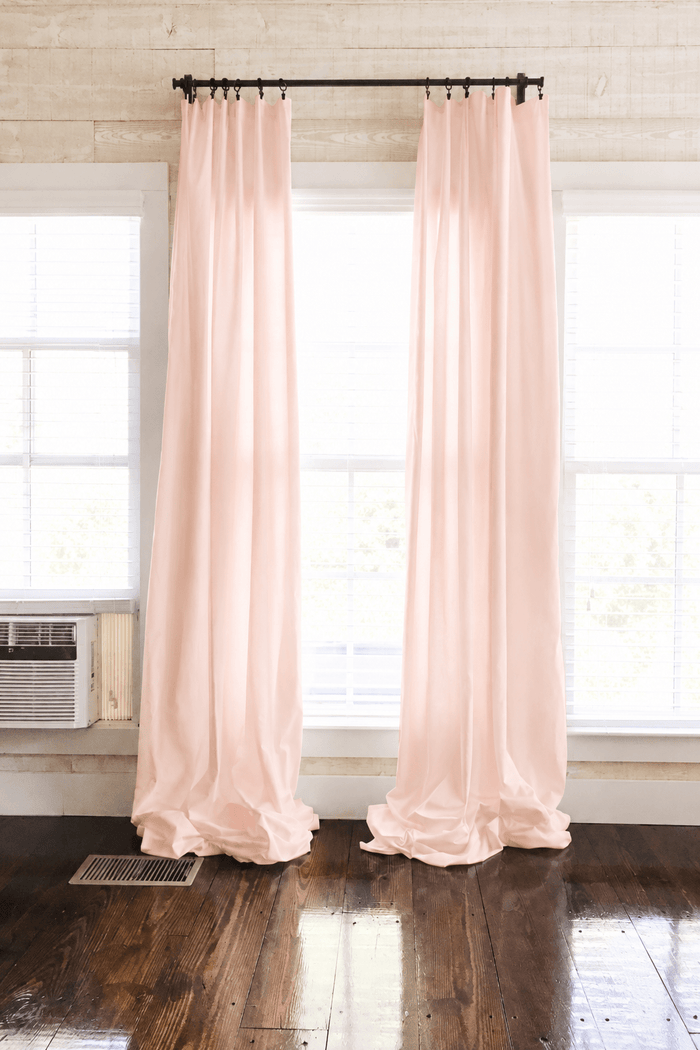 Ballet Slipper Pink farmhouse nursery curtains hung as two panels on a black rod, puddling on dark wood floors between white-trimmed windows - High Cotton Textile