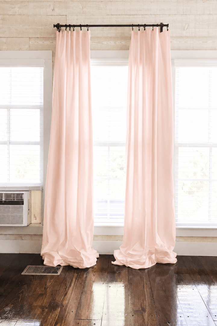 Ballet Slipper Pink farmhouse nursery curtains hung as two panels on a black rod, puddling on dark wood floors between white-trimmed windows - High Cotton Textile
