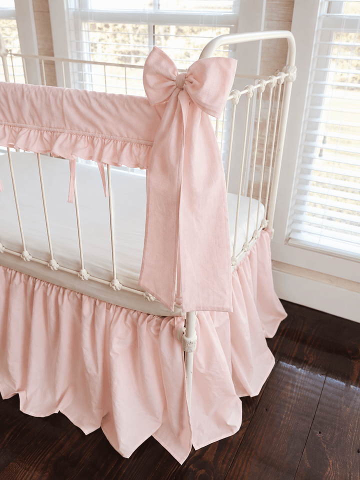 Close view of a Ballet Slipper Pink bow knotted at the crib post above the ruffled rail cover and farmhouse skirt