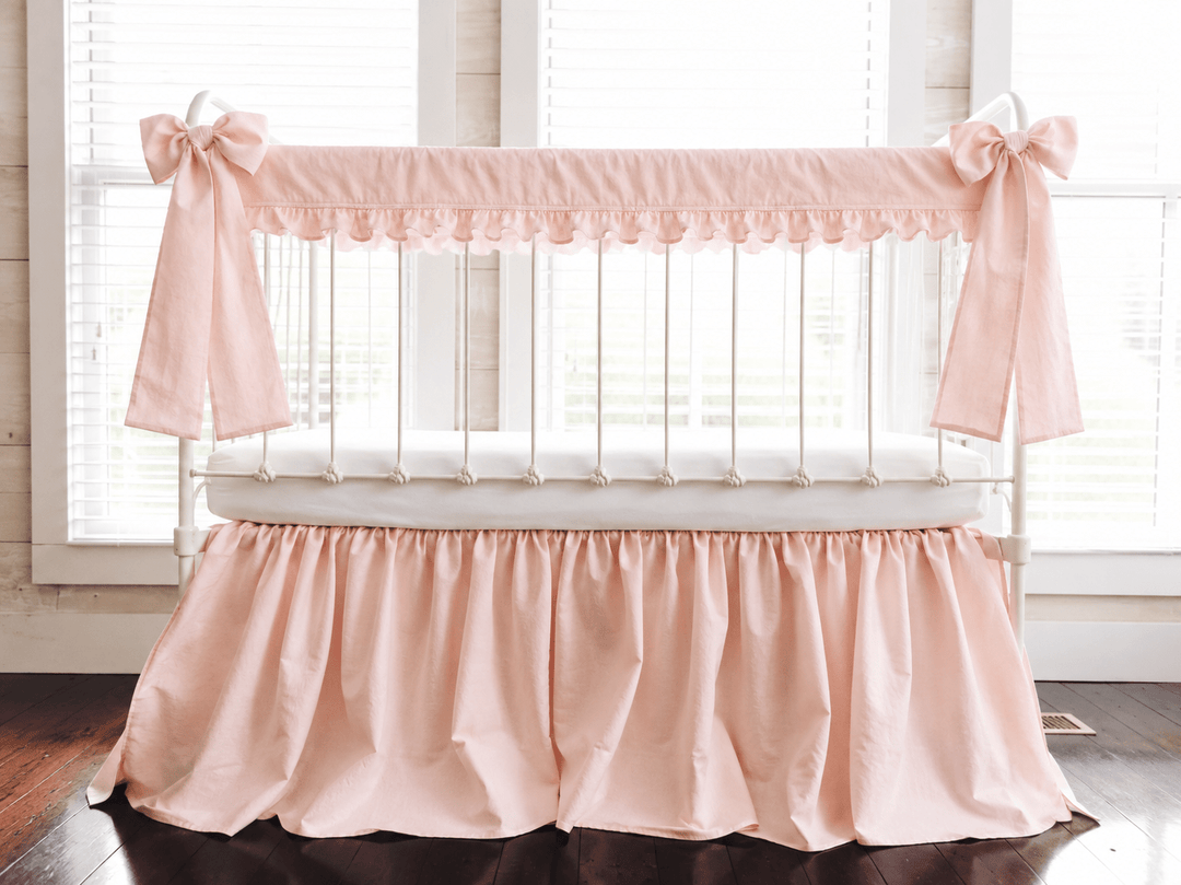 Ballet Slipper Pink ruffled crib rail cover, gathered farmhouse skirt and two long bows on a white iron crib, front view
