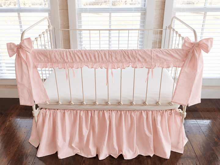 Straight-on view of the pink ruffled rail cover with slim ties between the spindles and a bow at each post