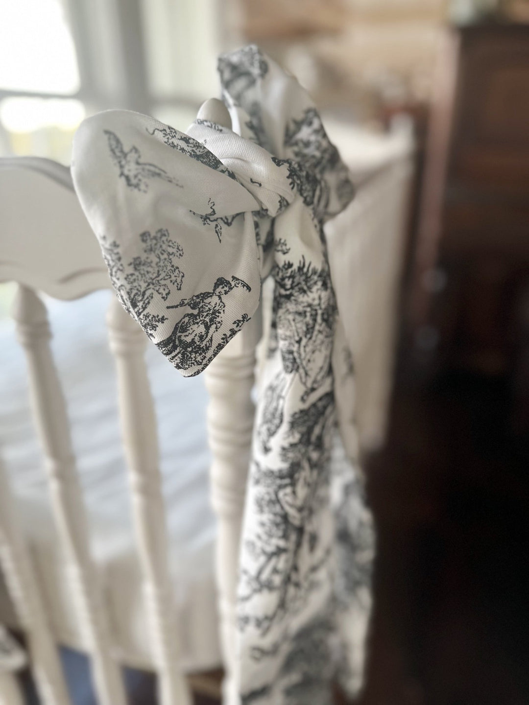 Side profile of a toile sash bow tied on a white crib