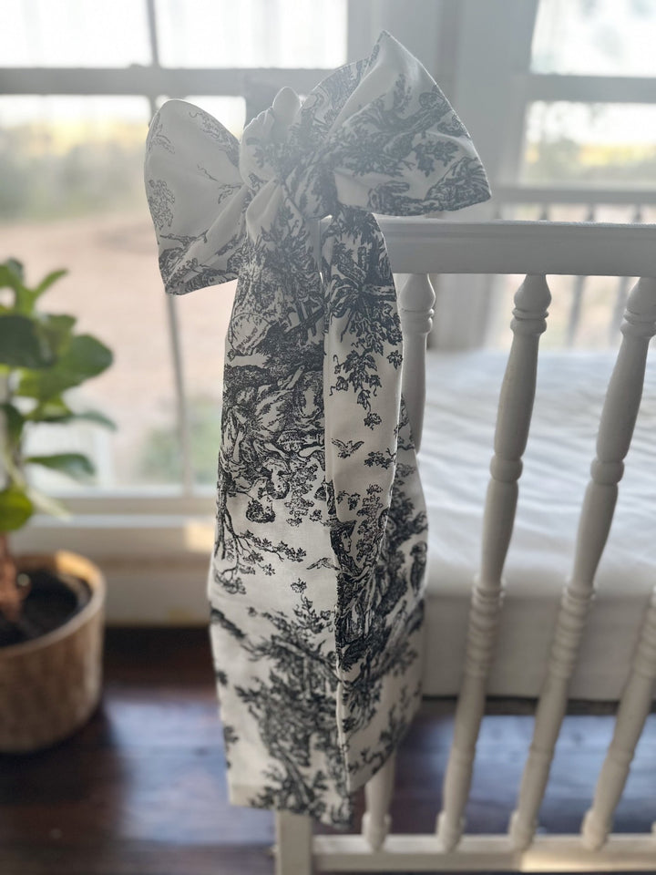 Tall black and white toile bow on a crib post with the tails reaching toward the floor