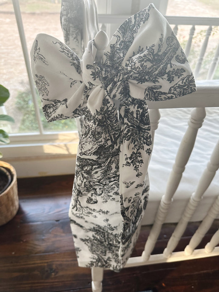 Full black toile bow tied on a white crib corner post by a sunny window