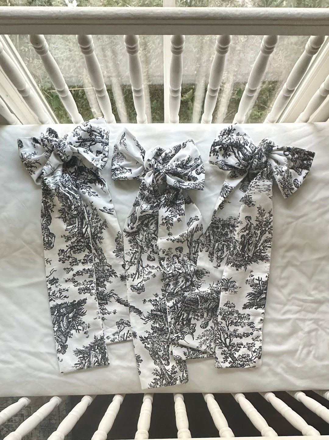 Three black and white toile bows laid flat on a white crib mattress