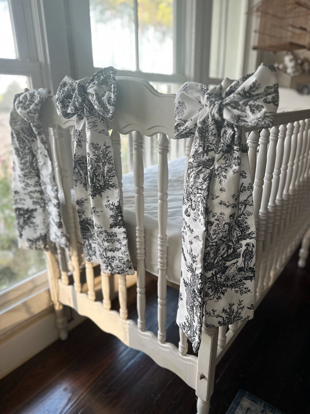 Black toile bows on the corner posts and side rail of a white crib in a sunlit nursery