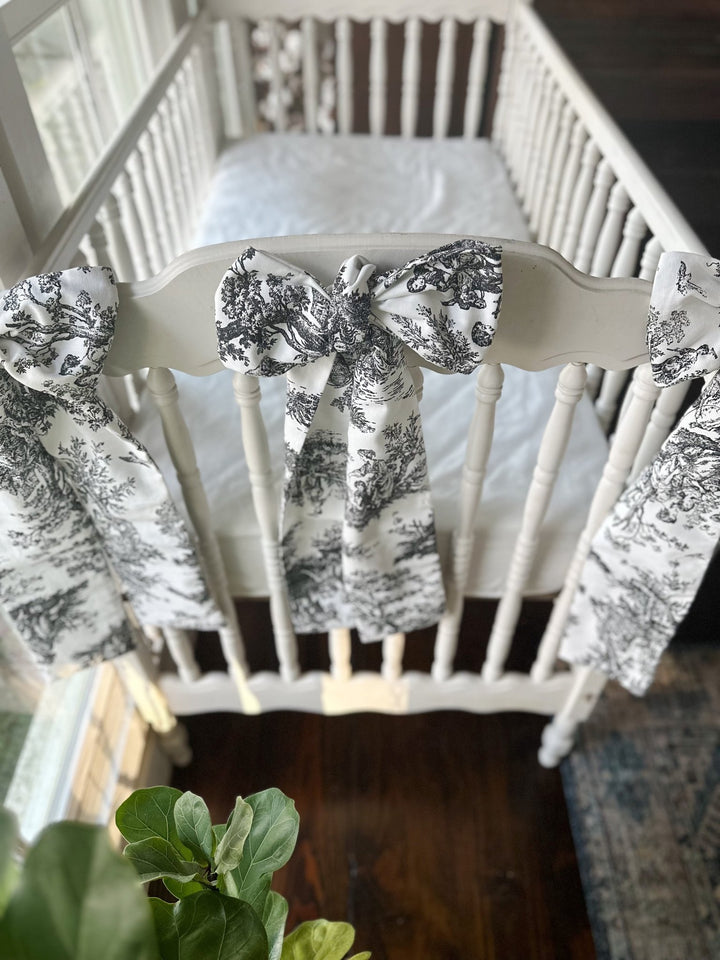 White spindle crib dressed with black toile bows on the footboard and both corner posts