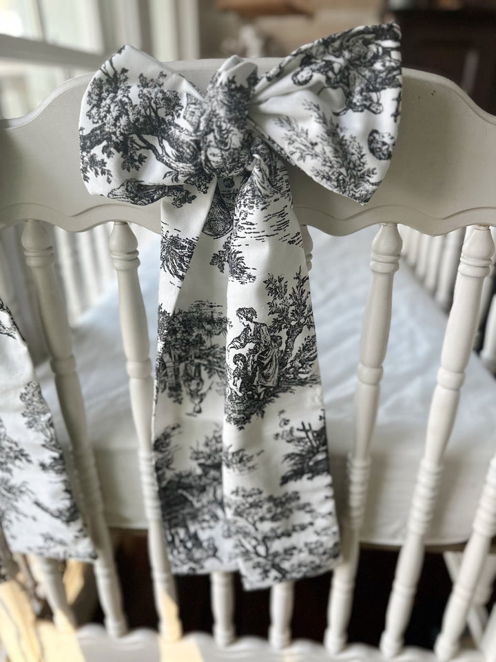 Toile bow tied across a white crib headboard with long printed tails