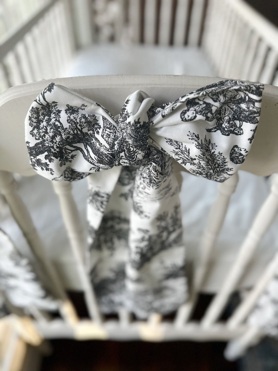 Black and white toile bow tied on the footboard of a white spindle crib, long tails hanging down