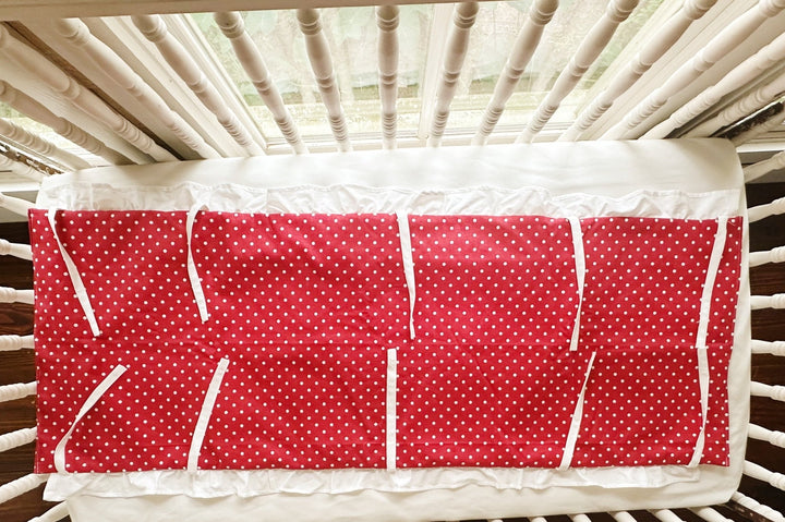 Red and white polka dot ruffled crib rail cover laid flat, white ruffle along the edge and every tie spread out
