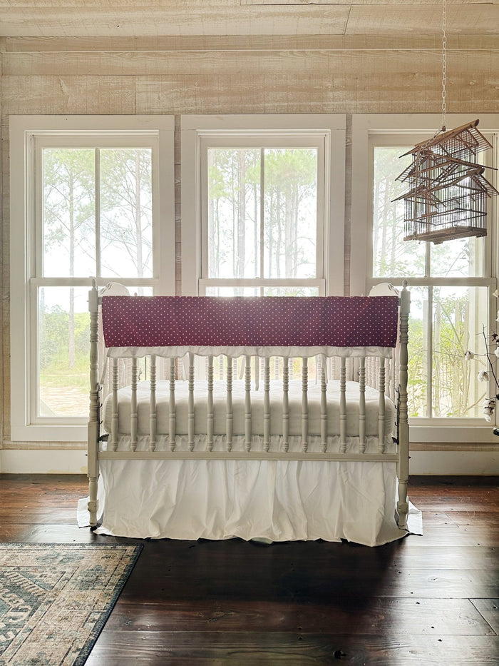 The two-piece red polka dot crib set in a pine-paneled nursery with three windows and a hanging birdcage